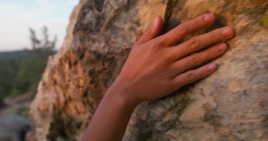 A persons hand rubs against a rock on top of a mountain