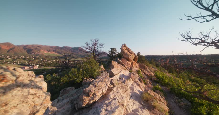 A rocky terrain is surrounded by grasses and trees at midday