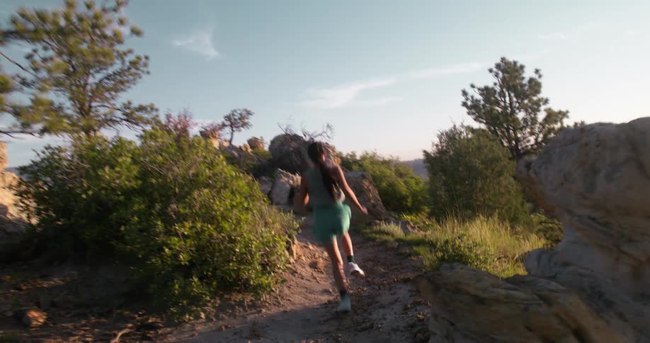 A woman trail running on a rocky and dirt path surrounded by trees and shrubs under a bright sky she is seen from different angles as she runs uphill showcasing the scenic rugged outdoor environment