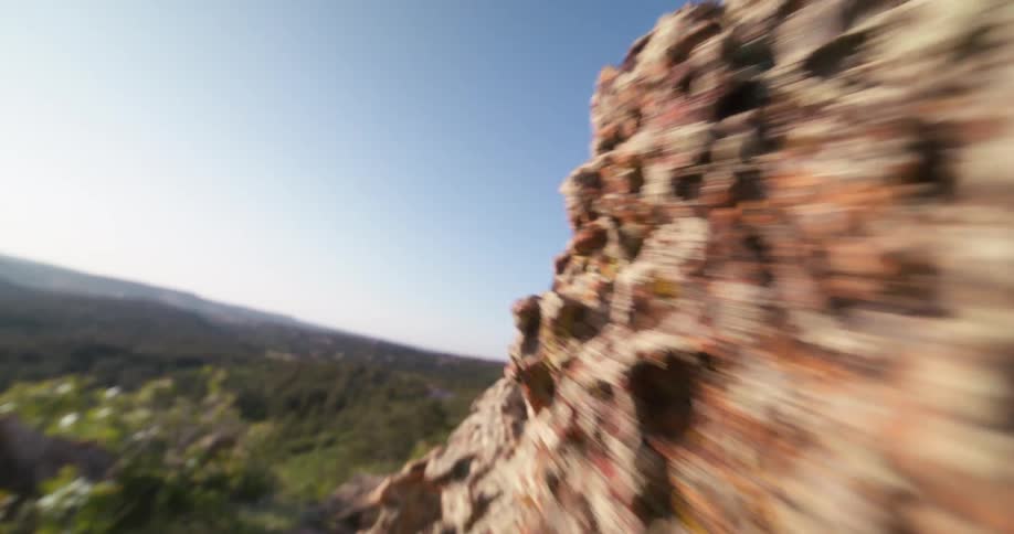 A swift pan glides over a rough mosscovered rock in the foreground revealing hills and a clear blue sky in the distance