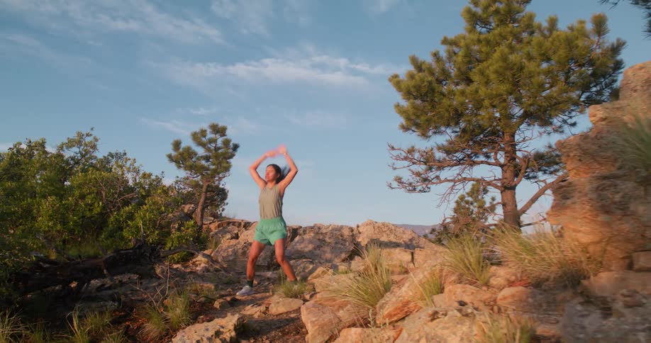 A woman does jumping jacks on a rocky trail surrounded by nature
