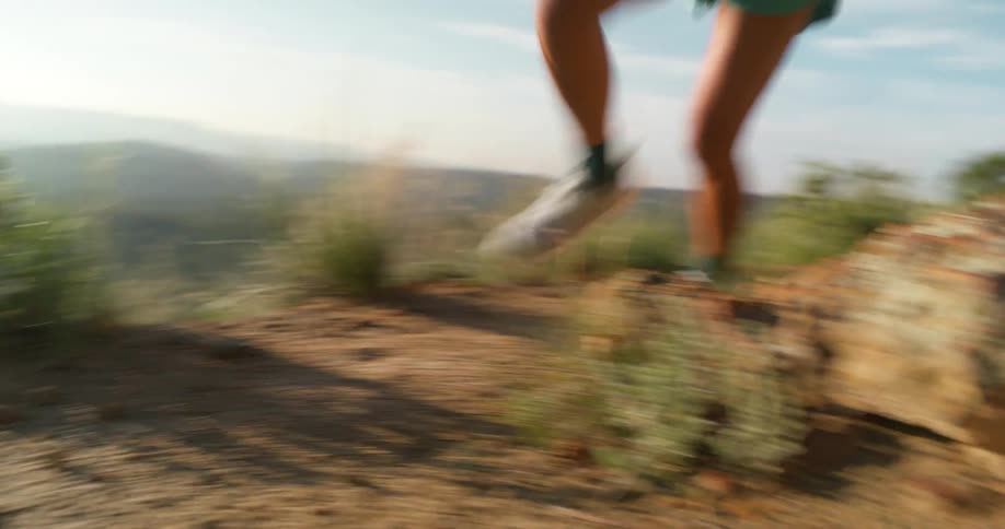 A woman runs on a mountain trail surrounded by vegetation