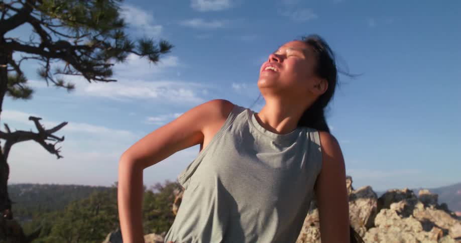 A teenage girl stands exhausted and breathing heavy atop a mountain