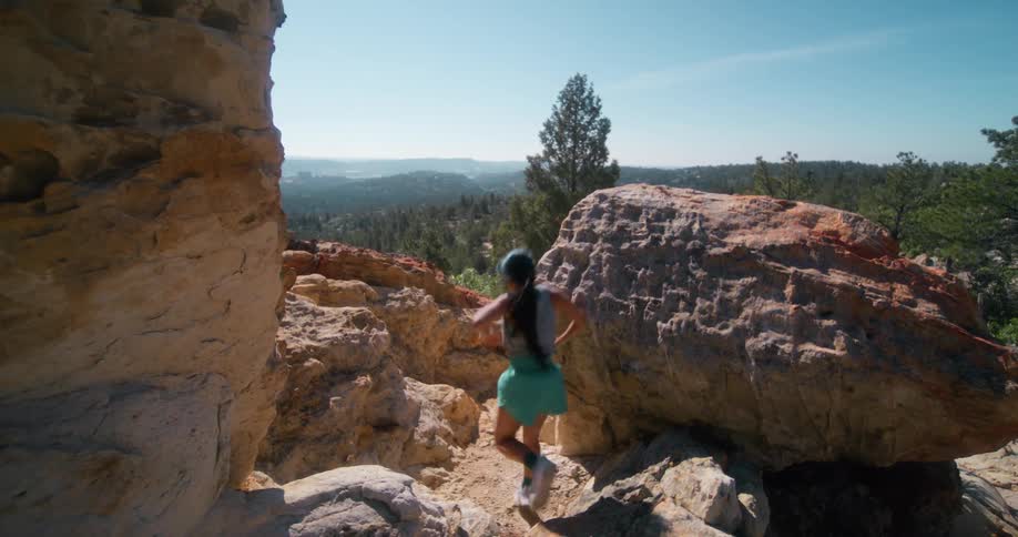 Woman running between rocks on a mountain trail