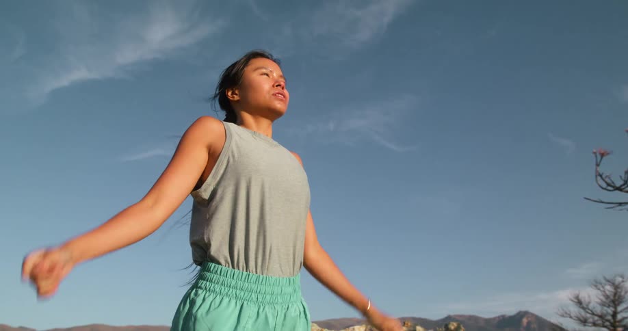 A woman stands peacefully on a rocky hilltop relaxing and enjoying the beauty of nature