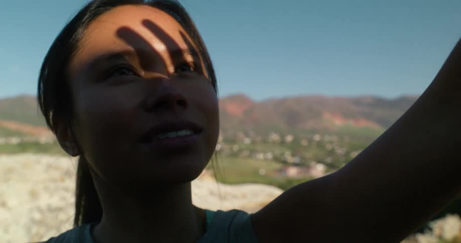 Woman with arm raised against the sun on a mountain trail