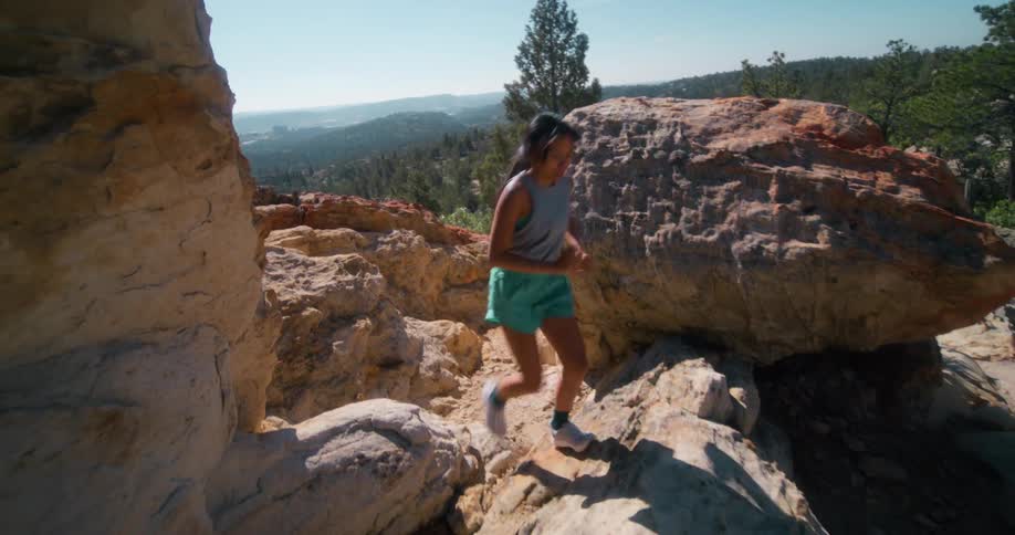 Woman running between rocks on a mountain trail