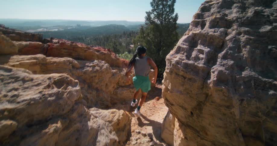 A young woman runs across rocky terrain at midday