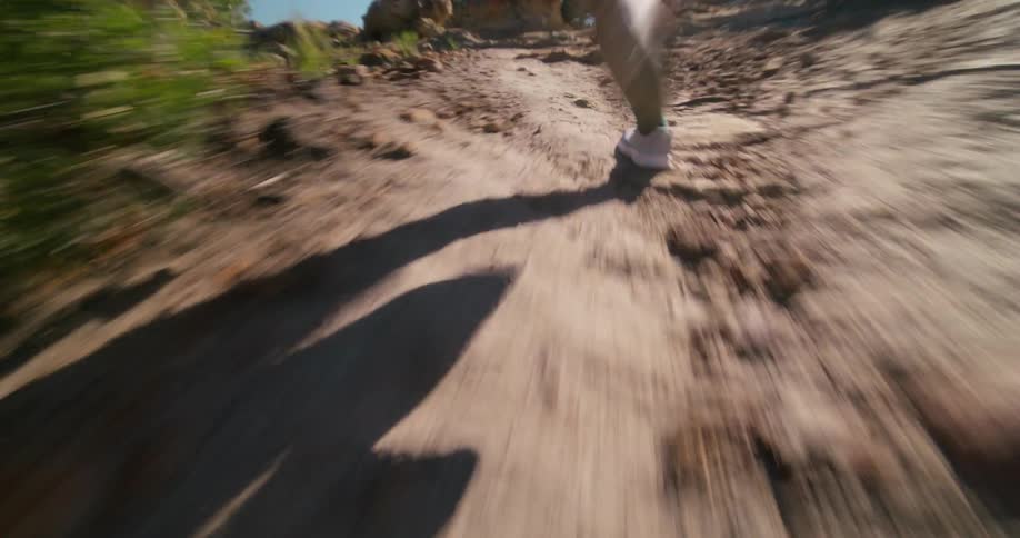 A person runs up a rocky trail through a sunlit forest
