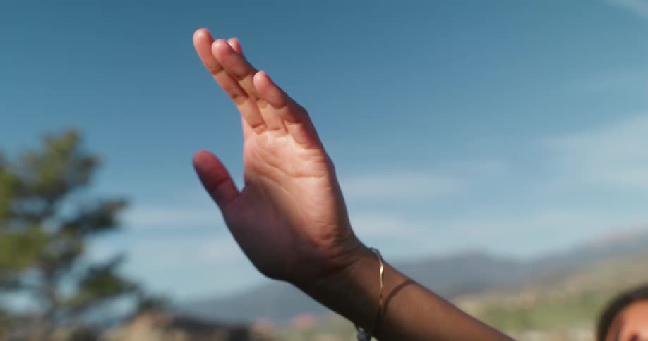 Woman on a mountain with her hand pointing towards the sun