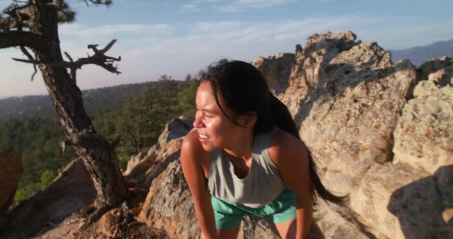 A young woman runs uphill to a rocky ridge and pauses to catch her breath
