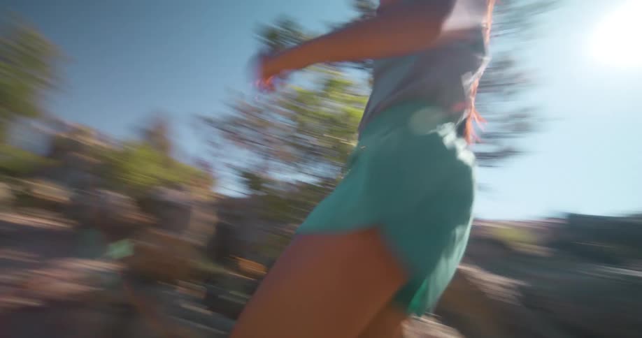 A woman runs on a rocky terrain at midday surrounded by trees