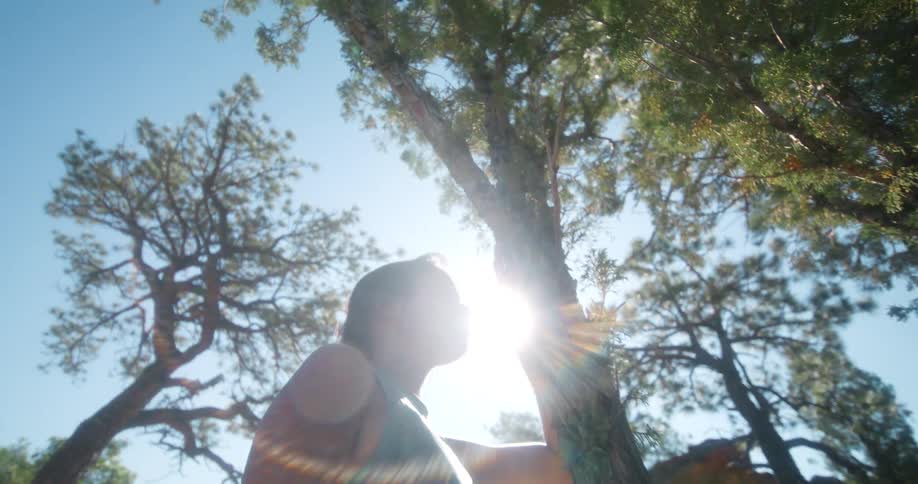 A young woman stands beside a tree catching her breath after a run at midday