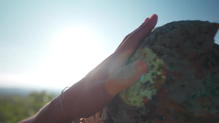 A persons hand running its palm over the surface of a stone outdoors on a sunny day