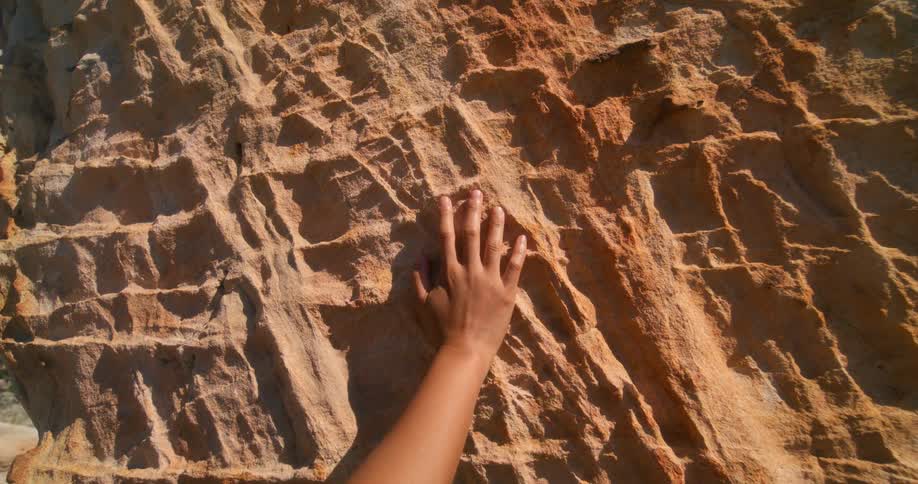 Persons hand touching a textured rock wall