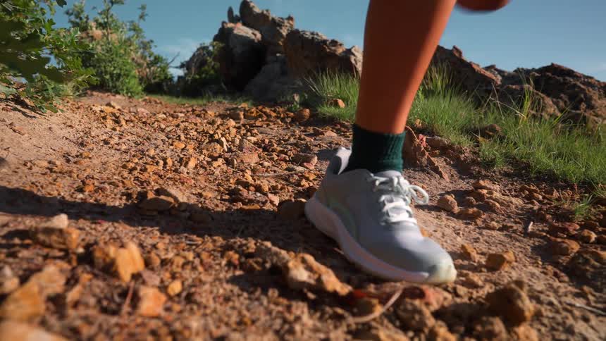 Legs of a woman running downhill on a mountain trail