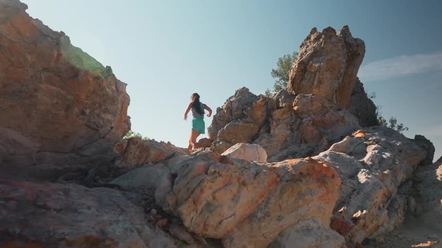 Woman in shorts running between rocks on a mountain trail