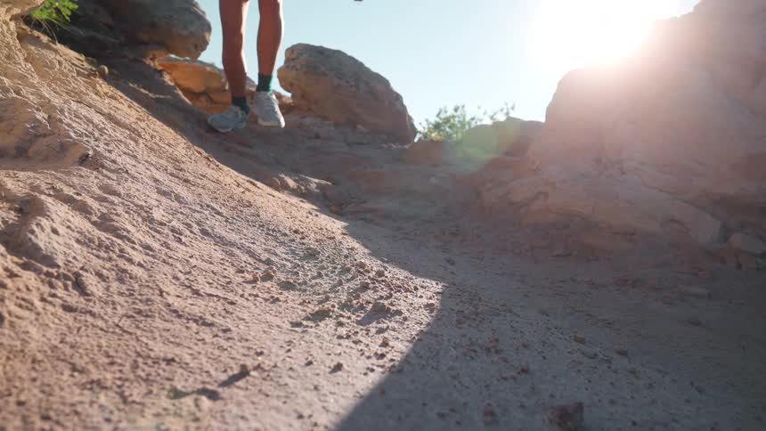 Woman runs down an arid sandy slope strewn with boulders on a sunny summer day