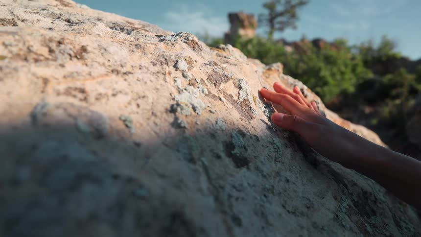 The person traces their hand on the boulder on a sunny day