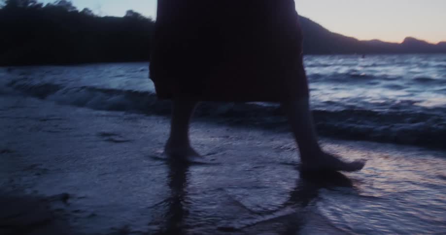 A female is walking on the beach at dusk