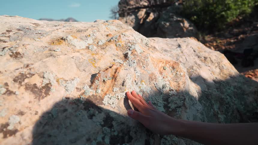 Arm stretched out and hand touching a rock outdoors