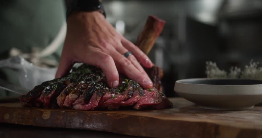 A chef slices a grilled steak on a wooden board