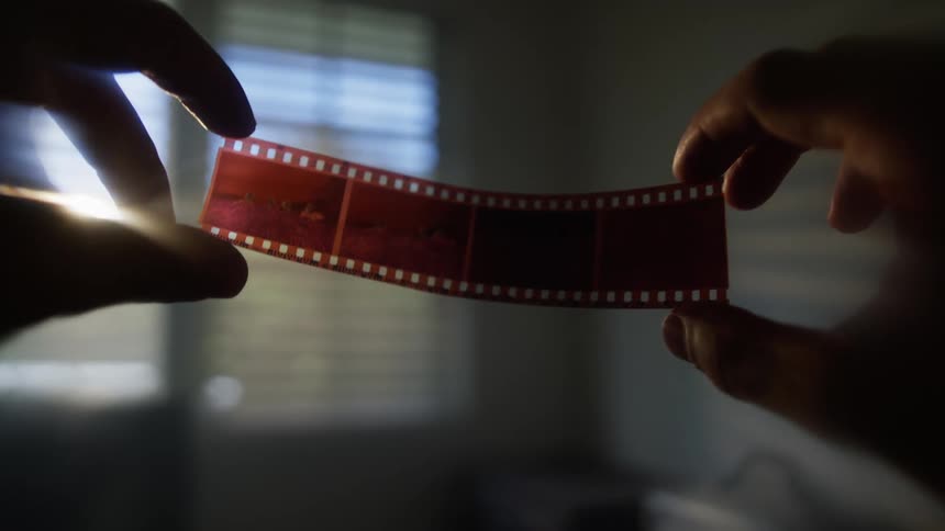 Close up of a short photography film held in the air by a person indoors during daytime