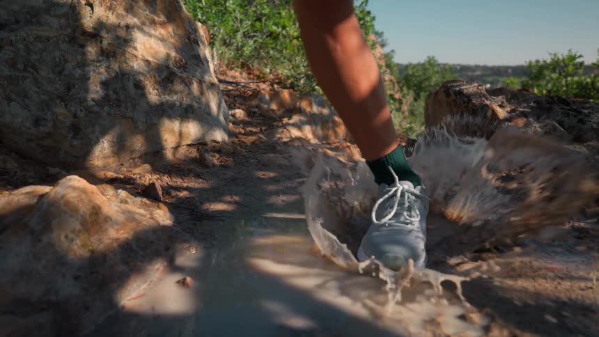 A woman splashes the puddle as she runs on the mountain trail