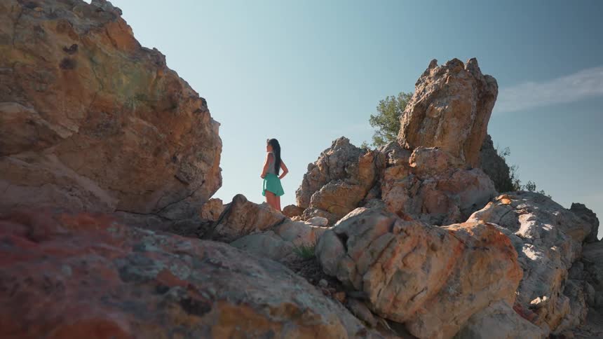A woman up on the rocks is looking at the view from the mountain top