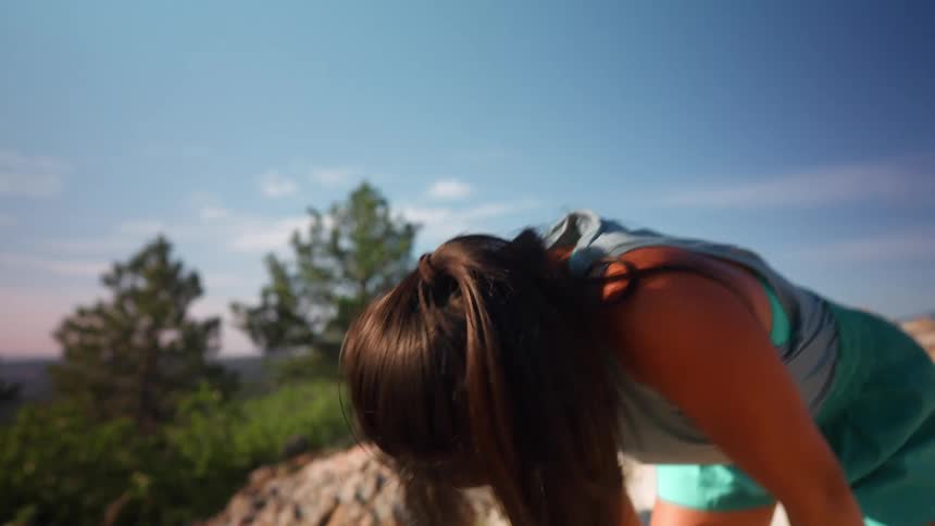 A woman runs to the top of the mountain and leans forward out of breath