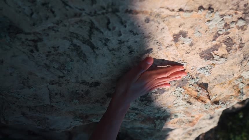 A persons arm rubs against a rock on a mountain at midday as the sun partially casts a shadow on the rock