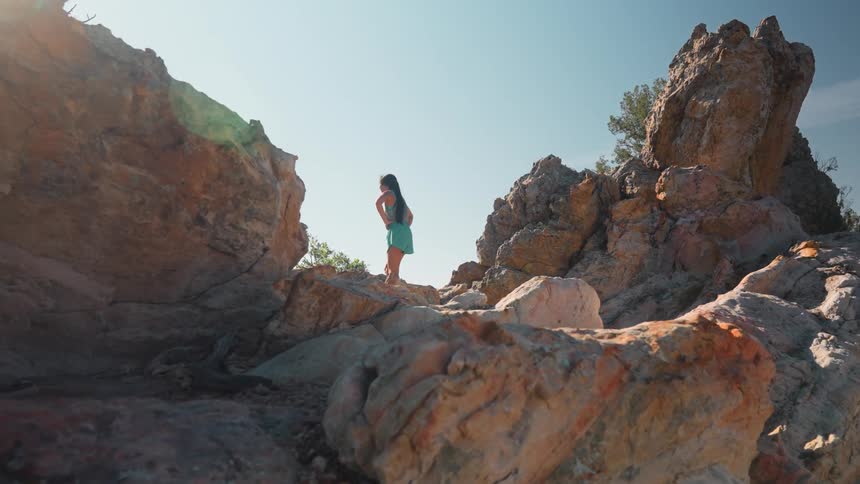 Woman in shorts running through rocky area and stopping at the top