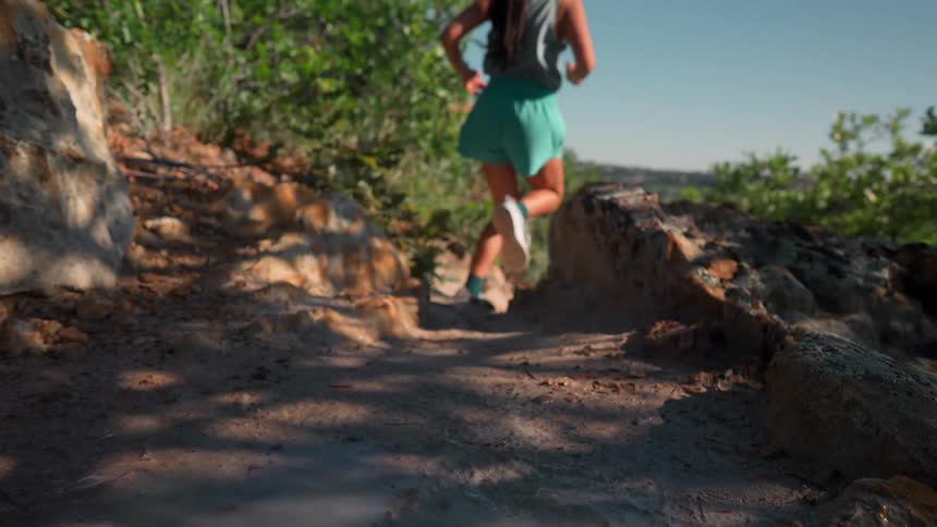 A woman in shorts and running shoes runs swiftly along an outdoor trail