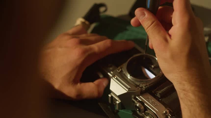Close up of a young man fixing screws in the lens area of a camera on a table top