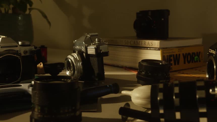 A warmly lit desk filled with vintage cameras lenses and photography books
