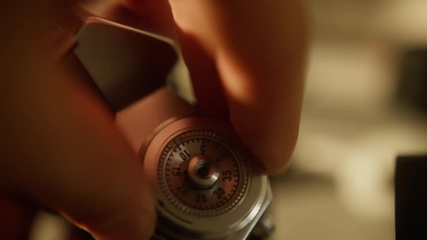 A persons fingers adjust a silver dial with numbers and arrows likely on a camera in a close view under warm light
