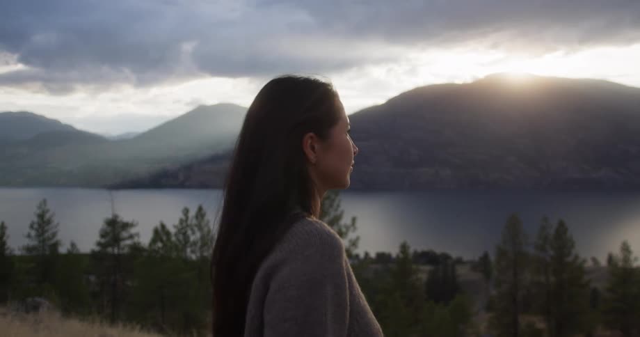 A woman looks out towards the water and mountains in front of her