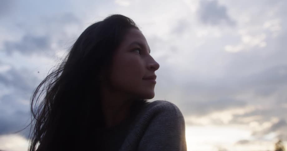 A woman looks up at the sky with a thoughtful expression as the clouds gather around her