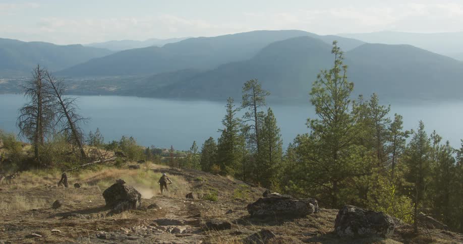 Female cyclist rides her bicycle over a rough slope near a forested lake shore