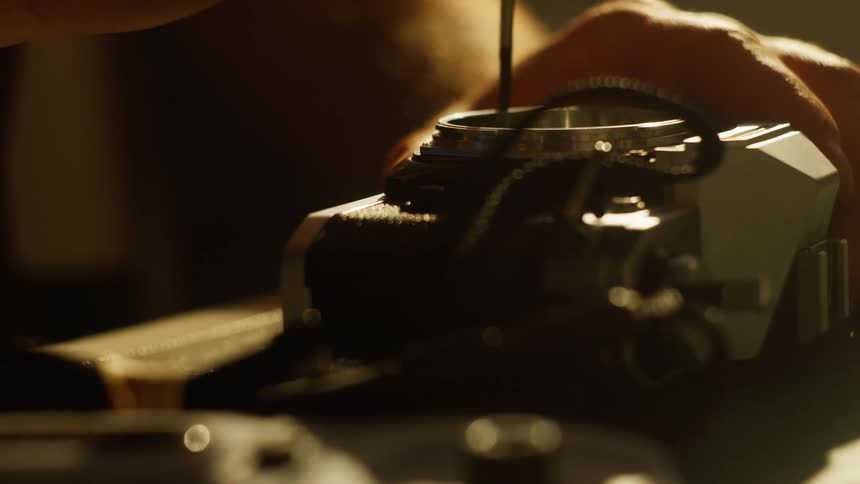 Close up of a man tightening screws on a camera with a screwdriver on a table surface