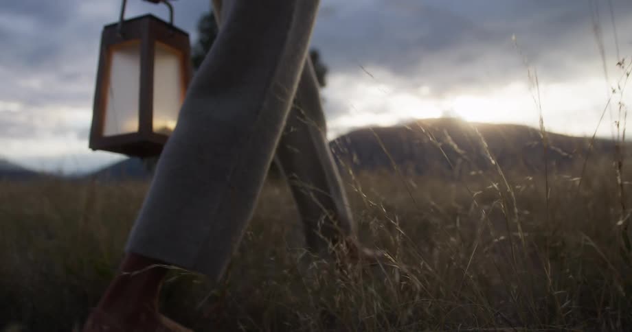 A woman walks barefoot on the grass while carrying a lantern