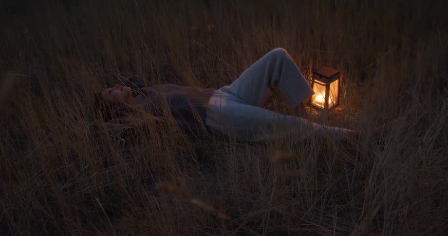 The woman lays by her lantern in the grass