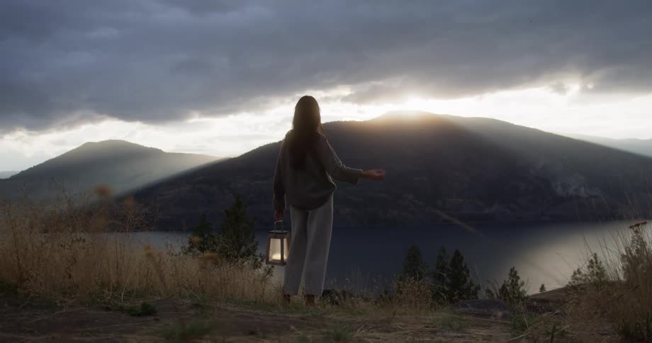 Woman with lantern overlooks lake and mountains at sunrise