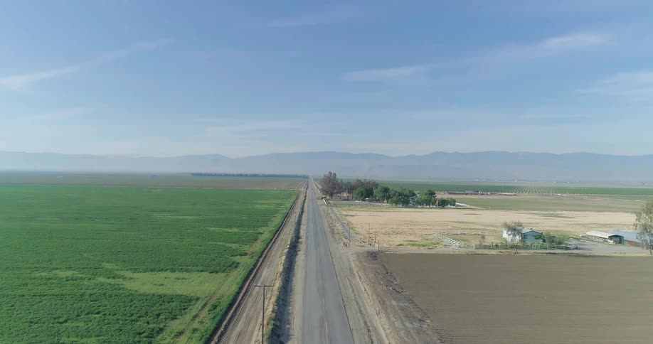 A long straight road stretches through vast farmland under a clear blue sky
