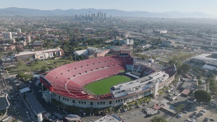 Aerial of Los Angeles Memorial Coliseum during daytime with the city skyline behind it