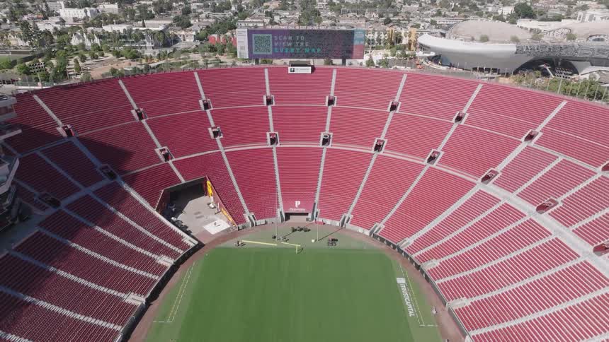 An aerial view of inside the Los Angeles Memorial Coliseum  with empty red seats and a digital scoreboard
