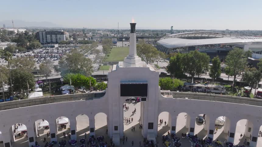 Los Angeles Memorial Coliseum  with red and white stands displays historical figures next to a monumental portico with columns and Olympic Torch caldron