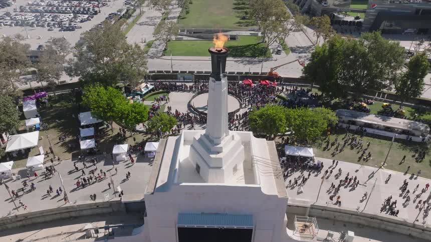 Aerial view of the lit Olympic torch on top of the Los Angeles Memorial Coliseum with people walking below