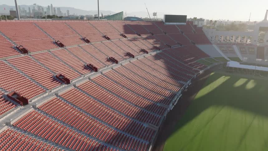 A large roofless football stadium sits empty with a green grass field in the center located in the middle of the city