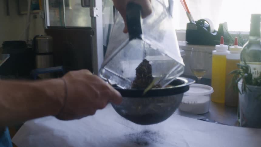 Person pours blended material into a strainer in a restaurant kitchen